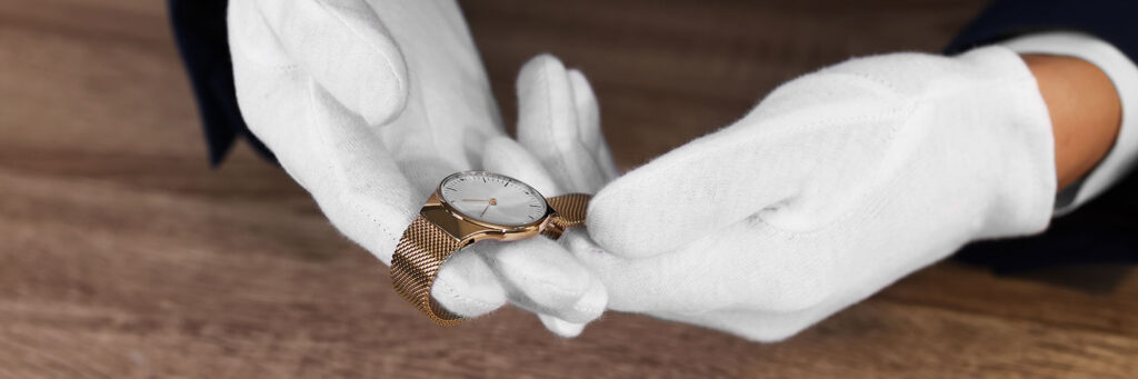man wearing white gloves holding a gold watch showing the process to sell your luxury watch