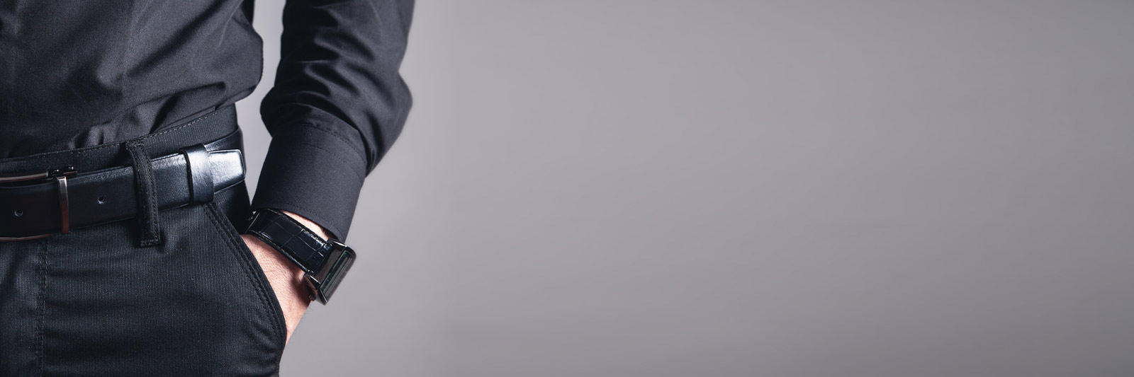 Man wearing a black luxury watch with hand in pocket against a gray background
