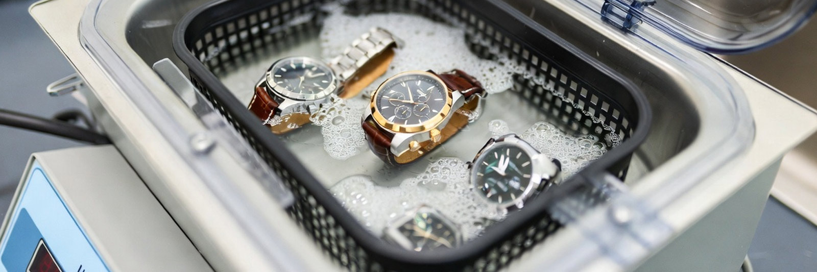 Several luxury watches being cleaned in a professional ultrasonic cleaning machine with soapy solution